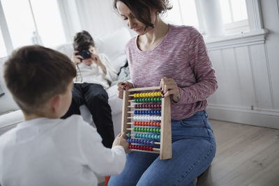 Mother holding abacus while son playing at home