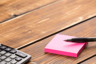 High angle view of pen with adhesive notes and calculator on wooden table