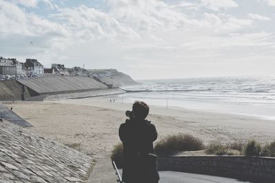 Rear view of man photographing through camera at beach