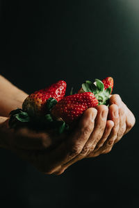 Midsection of person holding strawberry against black background