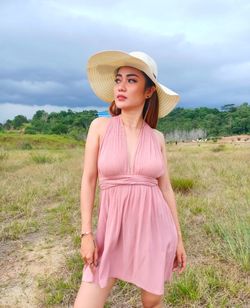 Beautiful young woman standing on field against sky