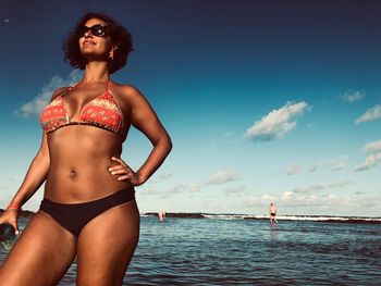 Woman in bikini standing by sea against sky