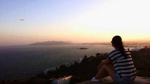 Rear view full length of woman looking at sea against sky during sunset