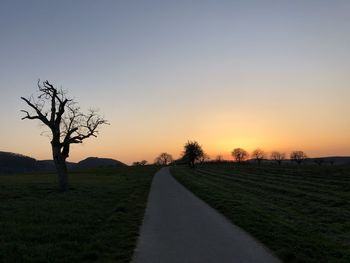 Road amidst field against clear sky during sunset