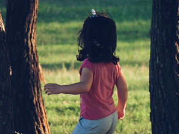 Rear view of girl standing amidst trees on grassy field