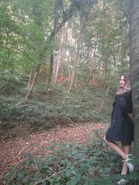 Young woman standing by tree in forest