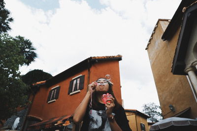 Low angle view of woman blowing bubbles in city against cloudy sky