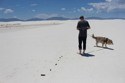 Rear view of man with dog walking on sand