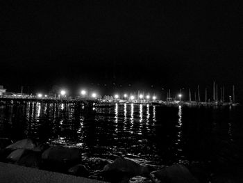 Illuminated city by river against sky at night