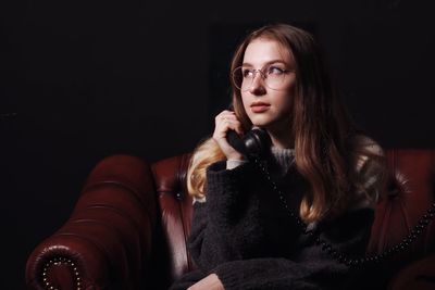 Portrait of beautiful young woman sitting against black background