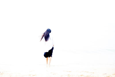 Rear view of woman standing at beach against sky