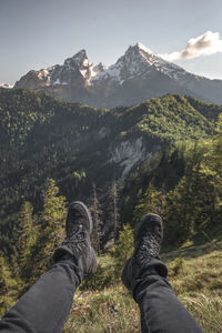 Low section of man sitting over mountain against sky