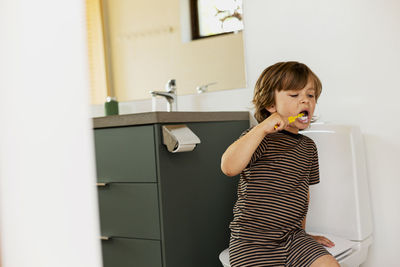 Boy brushing while sitting in bathroom