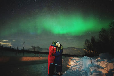 Rear view of photographing standing on snow against sky at night