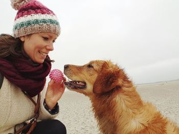 Close-up of smiling woman showing ball to dog at beach against sky