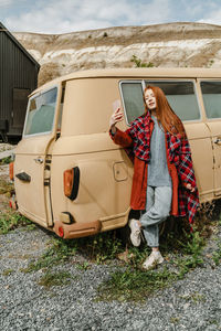 Young woman taking selfie leaning against van