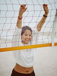 Portrait of happy woman holding volleyball net at beach