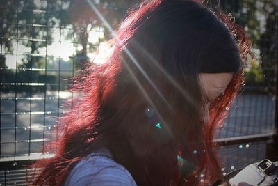 Close-up of sunlight falling on young woman by fence