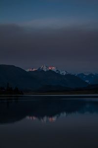 Scenic view of lake by snowcapped mountains against sky at sunset