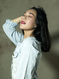 Young woman looking away while standing against wall