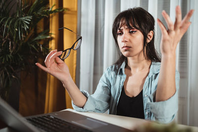 Frustrated young woman gesturing by laptop in office