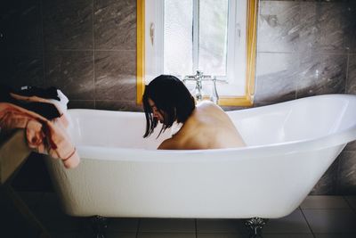 Shirtless woman sitting in bathroom at home