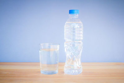 Glass of water bottle on table against blue background