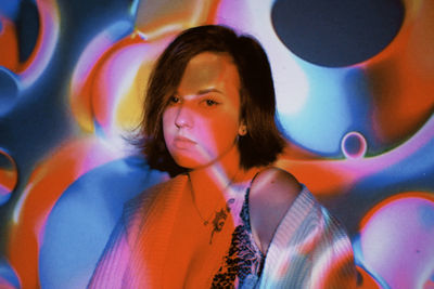 Portrait of beautiful young woman standing against multi colored background