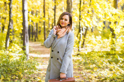 Young woman holding camera while standing in park