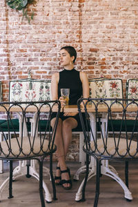 Full length of woman sitting on chair against brick wall