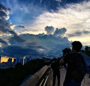 Rear view of man photographing against sky during sunset