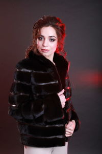 Fashionable young woman wearing fur jacket while standing against gray background