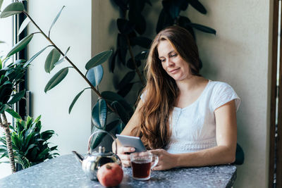 Young woman using phone while sitting on table