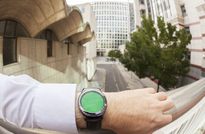 Cropped hand of businessman wearing wristwatch by railing in city