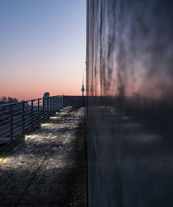 Walkway by building against sky at dusk