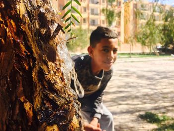 Boy hiding behind wet tree trunk