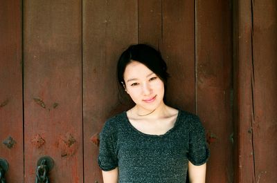 Portrait of smiling young woman standing against wooden door