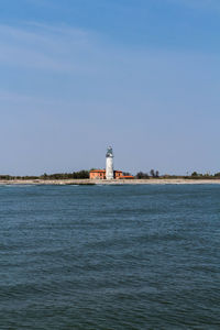 Lighthouse by sea against clear sky