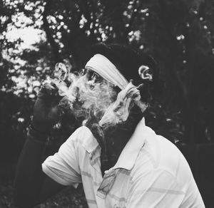 Side view of man smoking cigarette against trees