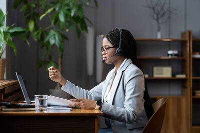 Confident afro businesswoman in headset at online video meeting hold documents discussing project