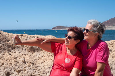 Friends taking selfie at beach against clear sky