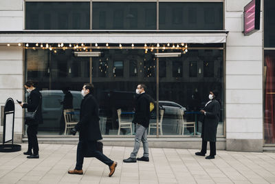 Businessman walking while male and female colleagues standing in line outside store during pandemic