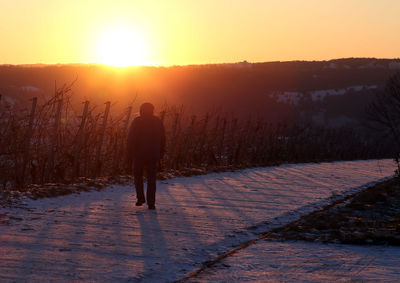 Rear view of silhouette person walking on snow covered landscape