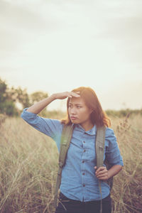 Beautiful young woman standing on field against sky