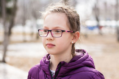 Young attractive serious girl in glasses in a city park in early spring looks into the distance