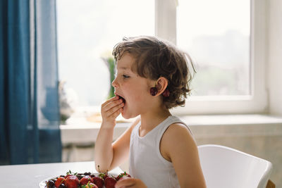 Cute beautiful little boy eating fresh cherry and strawberry.