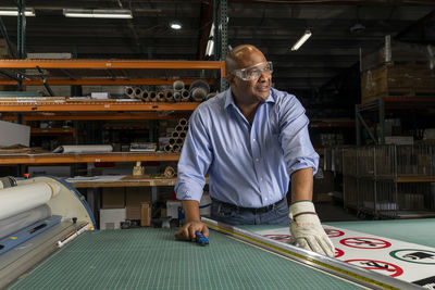 Smiling employee wearing protective eyewear looking away while working in print shop