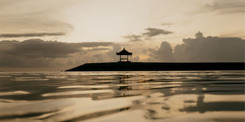 Silhouette building by sea against sky during sunset