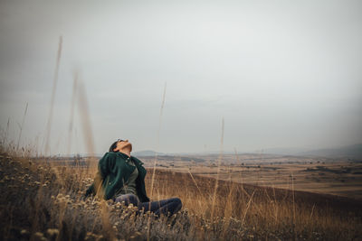 Woman sitting on field against sky