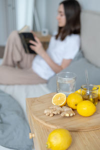 Lemons and ginger on table while woman sitting in background at home